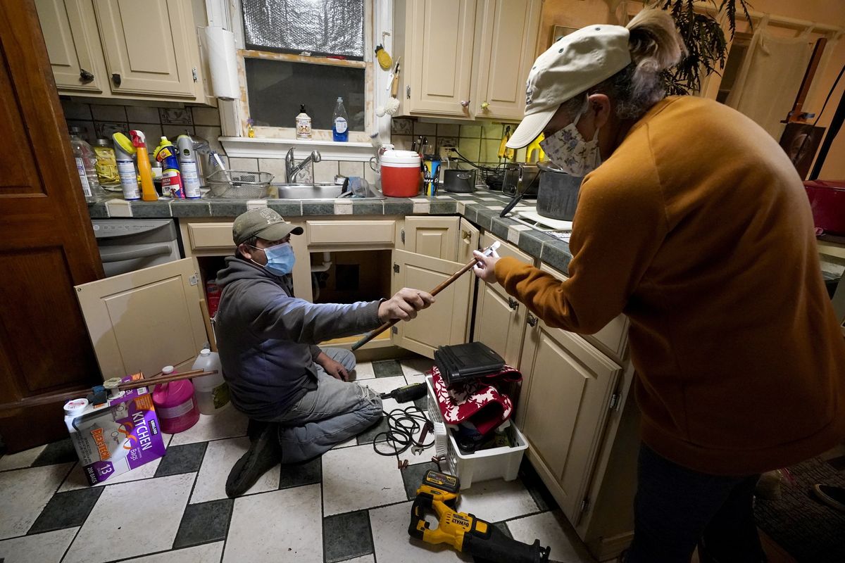 FILE - In this Feb. 20, 2021, file photo, Handyman Roberto Valerio, left, hands homeowner Nora Espinoza the broken pipe after removing it from beneath her kitchen sink in Dallas. The pipe broke during freezing temperatures brought by last week