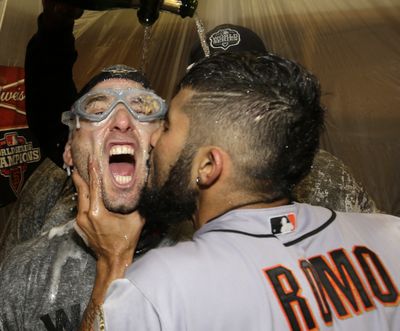 Sergio Romo kisses Marco Scutaro as they are sprayed with champagne during Giants’ clubhouse celebration Sunday night. (Associated Press)