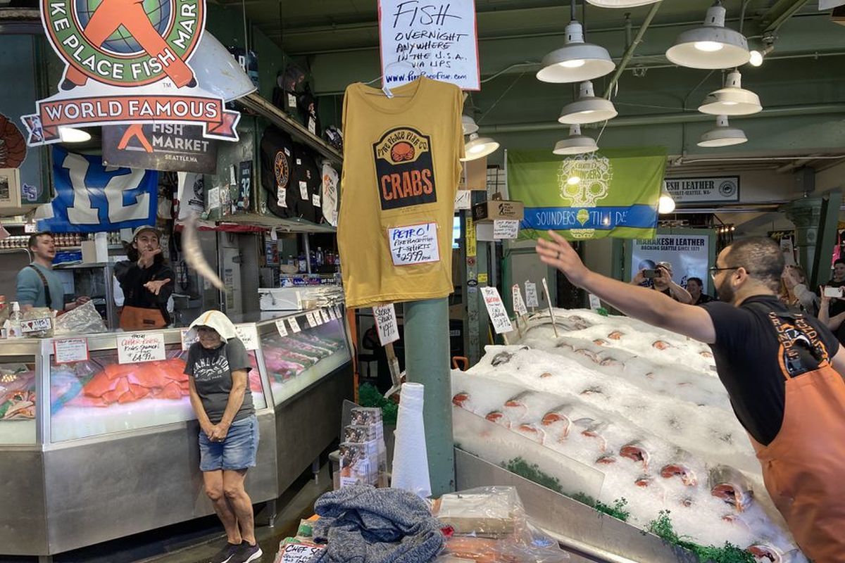 A visitor wears a towel on her head to avoid getting hit by flying fish at Pike Place Fish in Seattle.  (Tribune News Service)