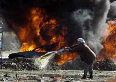 
A man pours water as he tries to prevent fire spreading from a burning tanker in Baghdad on Friday. An oil pipeline was sabotaged south of Baghdad on Friday, sending a huge plume of black smoke into the sky in the latest attack on Iraq's vital oil infrastructure. 
 (Associated Press / The Spokesman-Review)