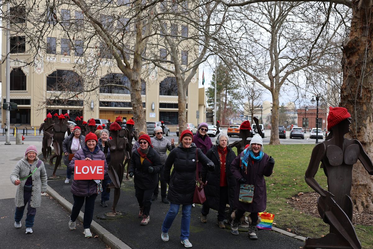 A group of passionate Spokane women who knitted red tasseled hats strike running poses among the Bloomsday runner statues on Tuesday, Feb. 24. The red hat resistance started in Norway during World War II as a way to peacefully and quietly protest the Nazi regime.  (Mathew Callaghan / The Spokesman-Review)