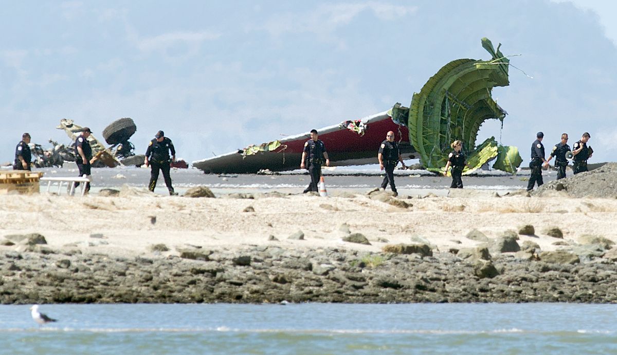 Investigators pass the detached tail and landing gear of Asiana Flight 214 after it crashed at San Francisco International Airport on Saturday. (Associated Press)