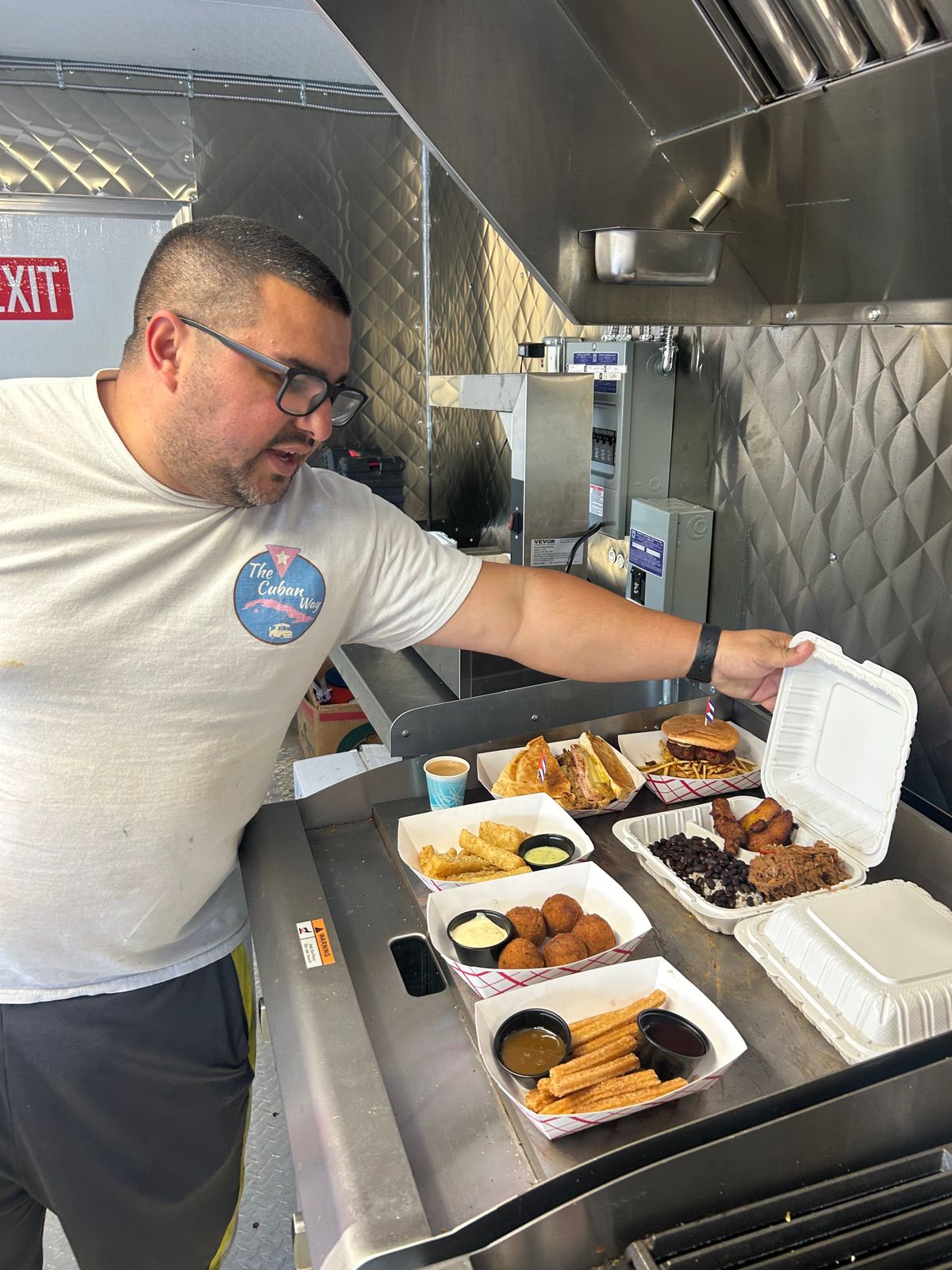 Jose Sosa proudly displays the assortment of food available for purchase at the Cuban Way food truck on Friday, May 8, in Spokane, Wash. Among the entrees up for grabs are frita burgers ($12), roasted pork sandwiches ($18), Cuban tamales ($16), ropa vieja ($18), vaca frita ($18), cuban steak ($18), churro fries ($8), and more.  (Mathew Callaghan / The Spokesman-Review)