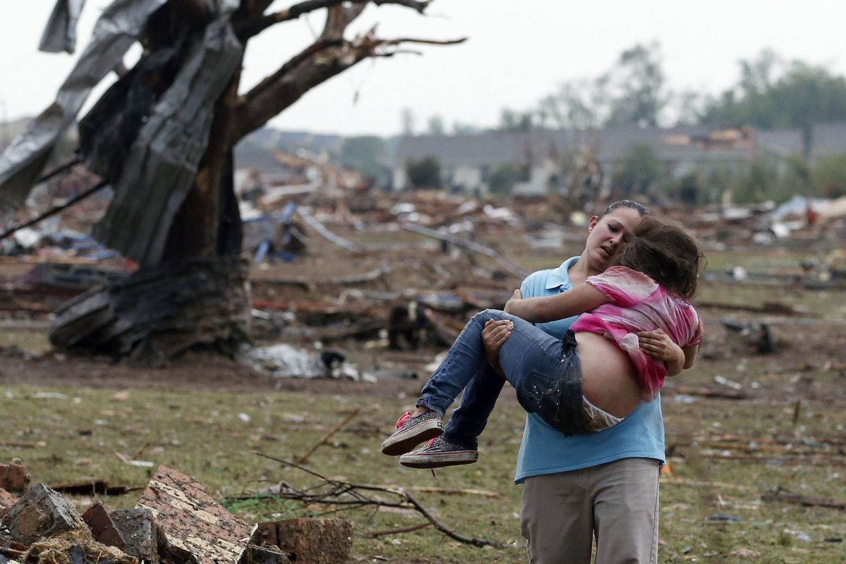 A woman carries a child through a field near the collapsed Plaza Towers Elementary School in Moore, Okla., Monday. A tornado as much as a mile wide with winds up to 200 mph roared through the Oklahoma City suburbs Monday, flattening entire neighborhoods. (Associated Press)