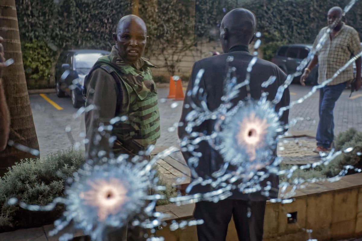 A member of the security forces is seen reflected in a window as he looks at bullet-holes, at a hotel complex in Nairobi, Kenya Tuesday, Jan. 15, 2019. Terrorists attacked an upscale hotel complex in Kenya