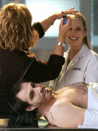 
Actor Gary Wayton looks toward the camera as he lays on an autopsy table playing a corpse while a makeup artist touches up actress Emily Procter on the set of 