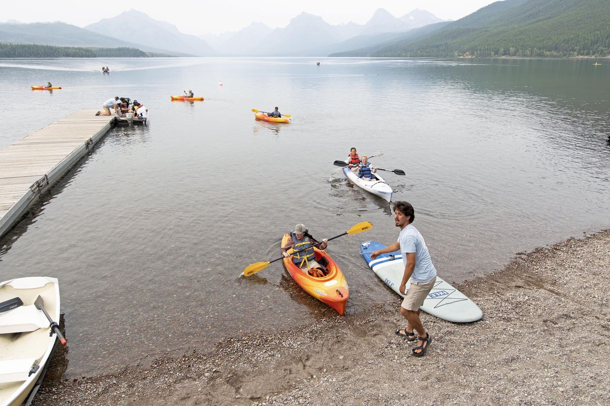 Isaiah Sullivan, the rental manager for the Glacier Park Boat Co., helps kayakers get into the water at Lake McDonald in Glacier National Park, Mont., on July 16. The Livingston Range in the distance is obscured by smoke from wildfires around the Pacific Northwest. MUST CREDIT: Photo by Justin Franz for The Washington Post.  (Justin Franz)