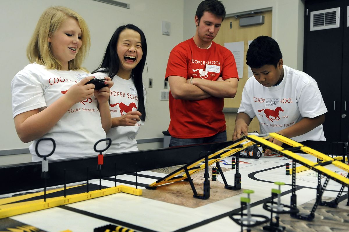 Competing has its fun side  for Trinh Nguyen and  teammates Brittnea Nelson, left, and Duy Vo, right,  at the  LEGO competition Saturday at Eastern Washington University. The Cooper Elementary students  test their transportation robot as coach Stefan Altberg looks on. (Dan Pelle)