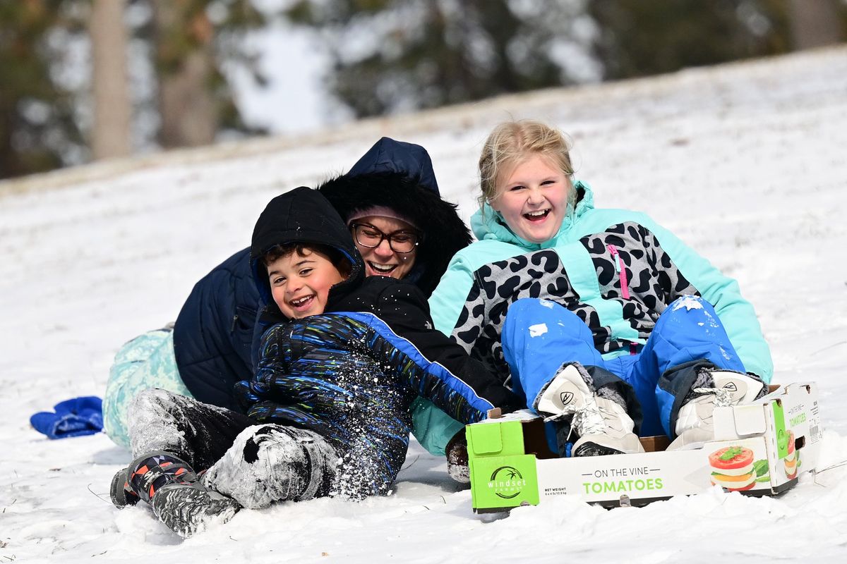 Gretchen Deutsch, center, pushes her son Keenan Rock and daughter Quinn Rock as they attempt to slide down a slope with improvised sleds on Wednesday at Audubon Park in Spokane.  (Tyler Tjomsland/The Spokesman-Review)