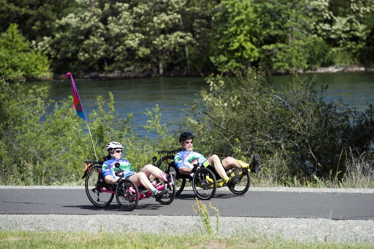 Debbie Claire, left, and Ron Spiewak ride their three-wheel recumbent bikes down the Centennial Trail near the state line and the Spokane River on June 6. (Jesse Tinsley)