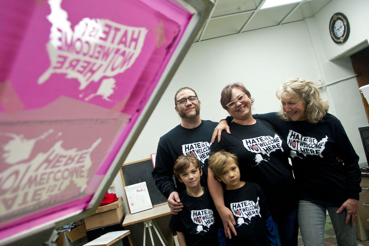 Local business owners Jeff Jacobs, back  left, and Randi Madison, center, along with their two children, Oscar, bottom left, and Scarlett, bottom center, talk with EWU professor Barb Brock,  right, about their “Hate Is Not Welcome Here” merchandise at Ammonite Ink, in Spokane on Wednesday, Nov. 29, 2017. The merchandise is in response to crimes against Norris Colley, a black man who was called racial slurs, threatened, and then shot at while at his home. (Kathy Plonka / The Spokesman-Review)