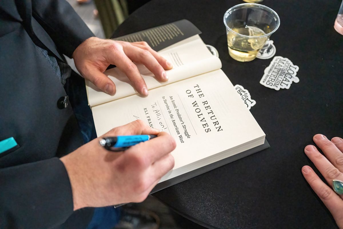 Spokesman-Review journalist and author Eli Francovich signs a copy of his new book “The Return of Wolves,” for Allison Burton at a VIP Northwest Passages pre-function, Thursday, April 13, 2023.  (Colin Mulvany/The Spokesman-Review)