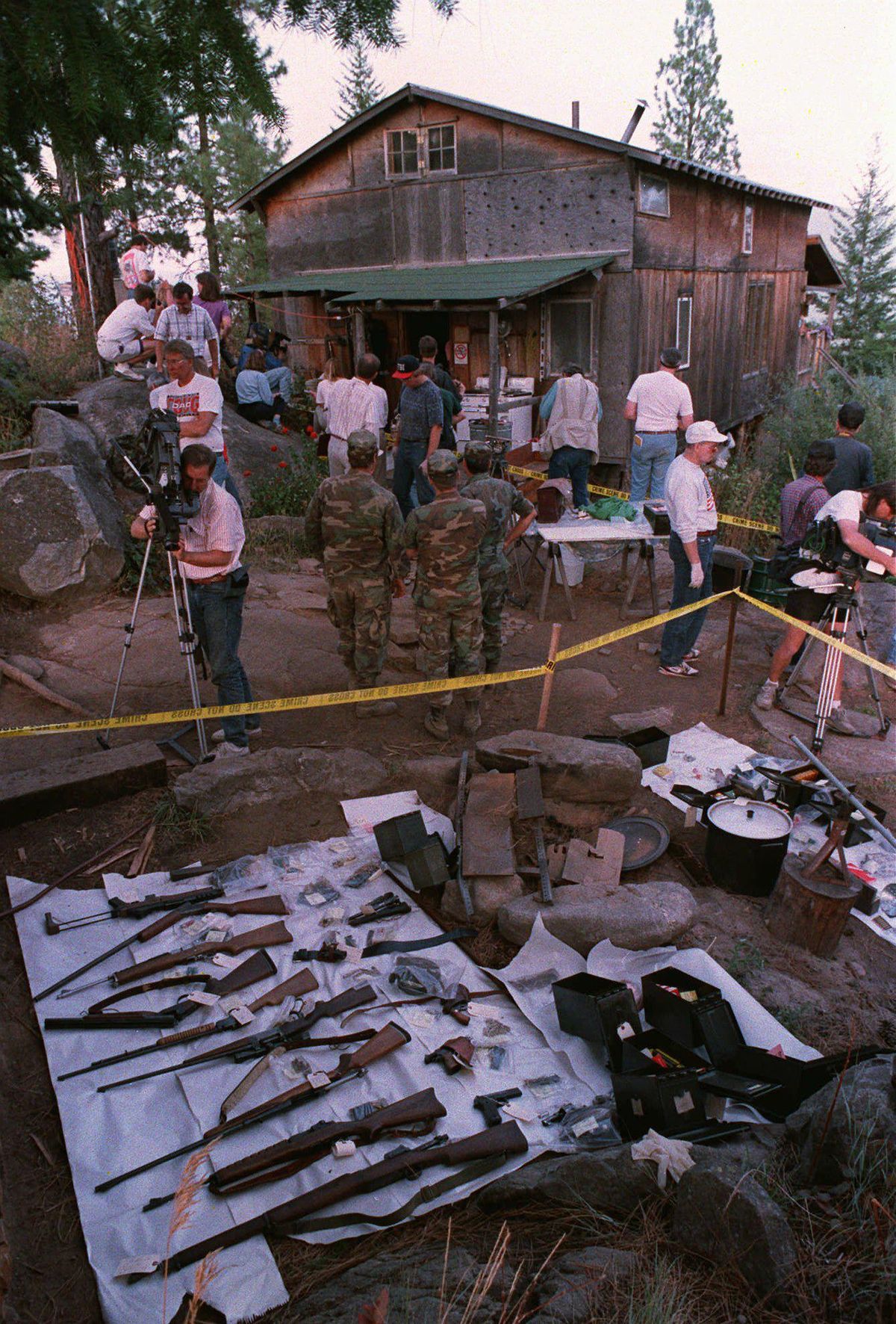 FILE – Federal agents and members of the media tour the outside of Randy Weaver’s home Sept. 1, 1992 near Naples, Idaho. Confiscated guns and ammunition are displayed on the ground following the end of the 11-day standoff. (GARY STEWART / ASSOCIATED PRESS)