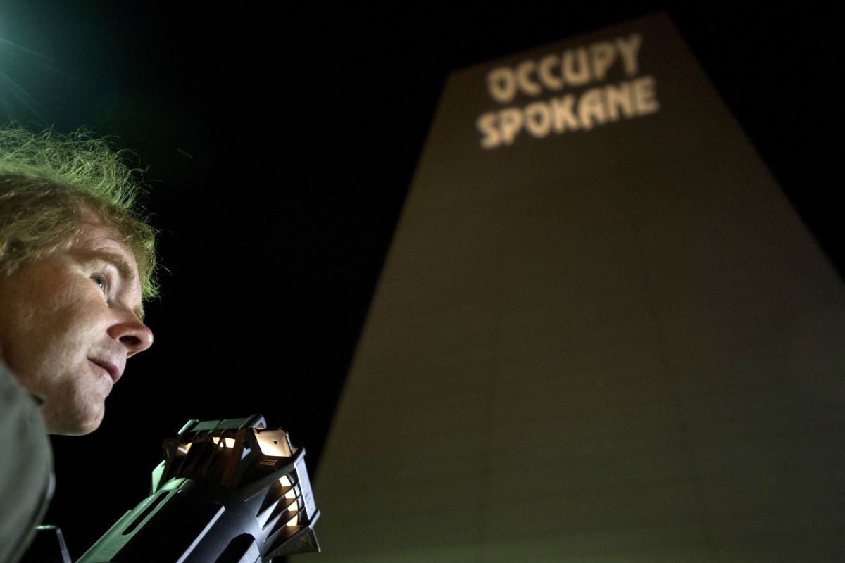 Ziggy, an activist with Occupy Spokane, uses a theater-grade light to project a message on the east side of the Wells Fargo Center on Wednesday in downtown Spokane. The message was visible looking west at the skyline and by motorists traveling westbound on I-90. (Tyler Tjomsland)