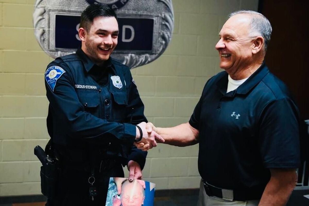 South Bend police officer Matthew Hegedus-Stewart, left, and retired South Bend Police Lt. Gene Eyster meet for the first time at the South Bend Police Department on March 22. Hegedus-Stewart is holding a picture of himself from Dec. 22, 2000, the day he was abandoned at 2 days old.