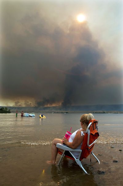 Jody Erickson, of Kent, Wash., watches the Colockum Tarps fire from her beach chair Monday while sitting on the bank of the Columbia River at the Crescent Bar Resort south of Malaga, Wash. (Associated Press)