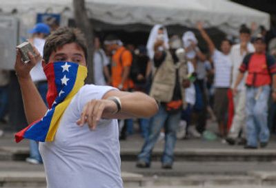 
A student, his face covered by a Venezuelan flag, throws a rock toward riot police Monday in Caracas. 
 (Associated Press / The Spokesman-Review)