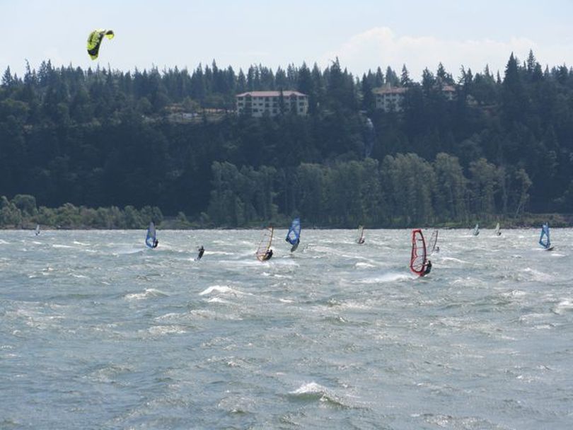 Windsurfers and a kitesailor enjoy a warm, windy day in the Columbia River Gorge on Tuesday. This photo was taken from the Spring Creek Fish Hatchery in Washington, looking across the river toward Hood River, Ore. and the Columbia Gorge Hotel and waterfall. (Betsy Russell / The Spokesman-Review)