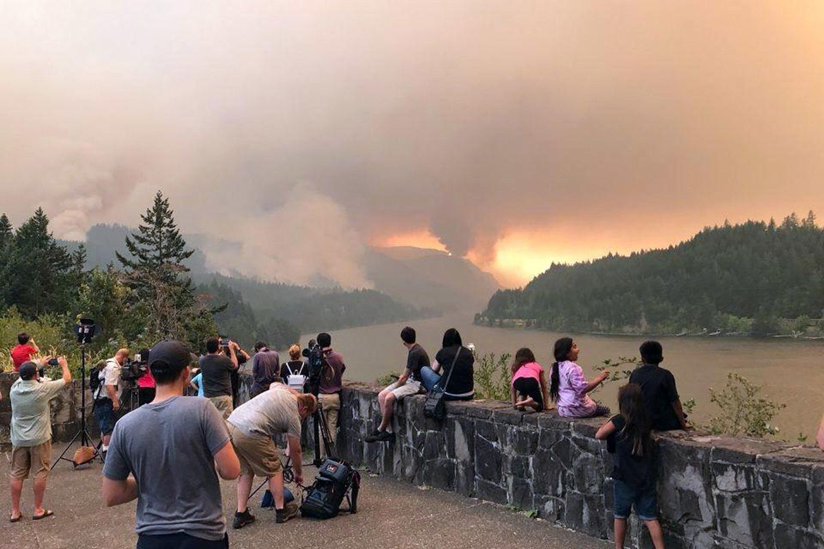 People at a viewpoint overlooking the Columbia River watch the Eagle Creek wildfire burning Sept. 4, 2017, in the Columbia River Gorge east of Portland, Ore., in this photo provided by Inciweb. (Uncredited / AP)
