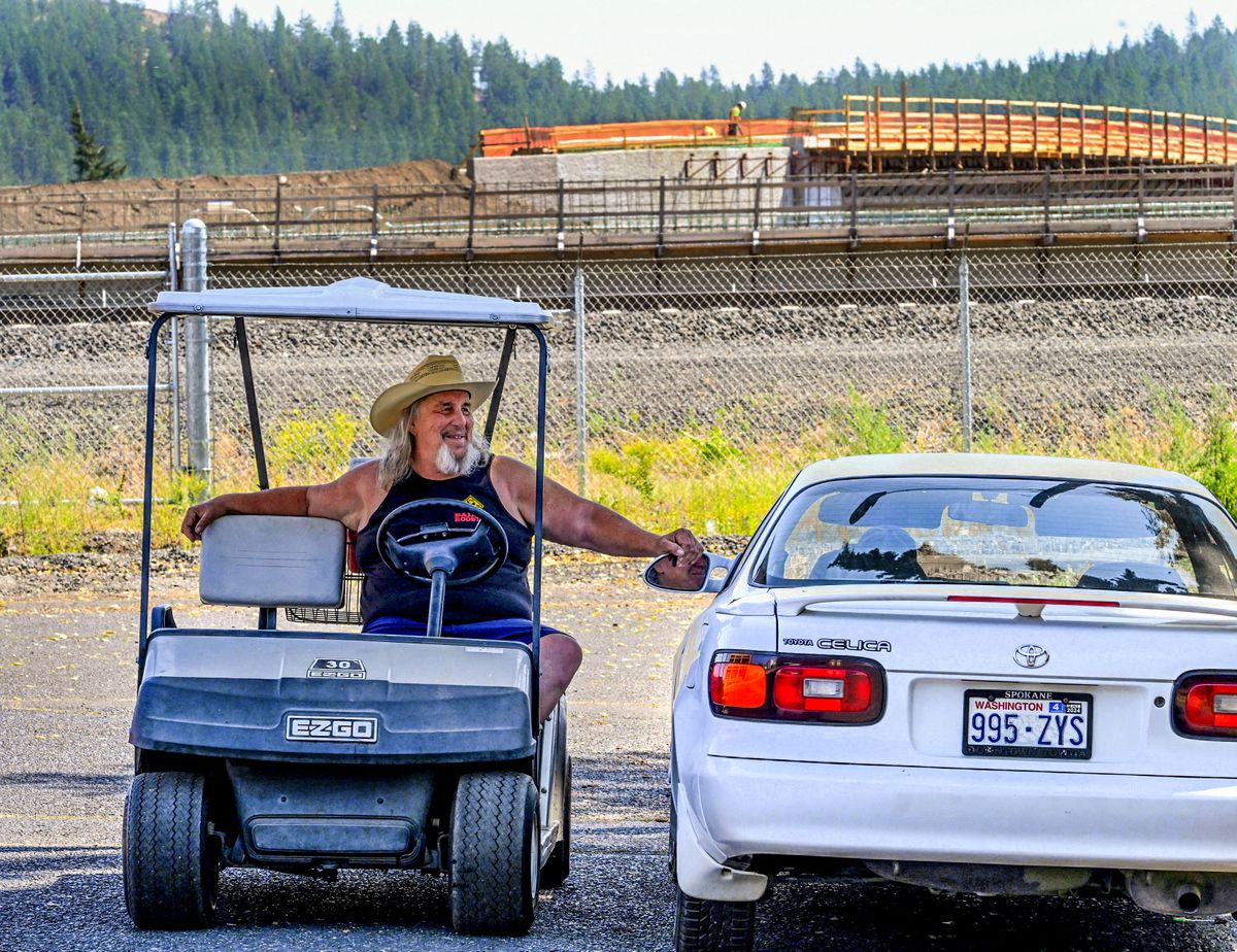 While listening to Led Zeppelin’s “Stairway to Heaven” in his golf cart, Paul Hamilton, the self-proclaimed “unofficial Sheriff of Hillyard,” chats with a neighbor near the corner of Greene Street and Olympic Avenue on Aug. 3 as the North Spokane Corridor northbound ramp is under construction in the background. Hamilton died Monday, Aug. 7 at 66 years old.  (DAN PELLE/THE SPOKESMAN-REVIEW)