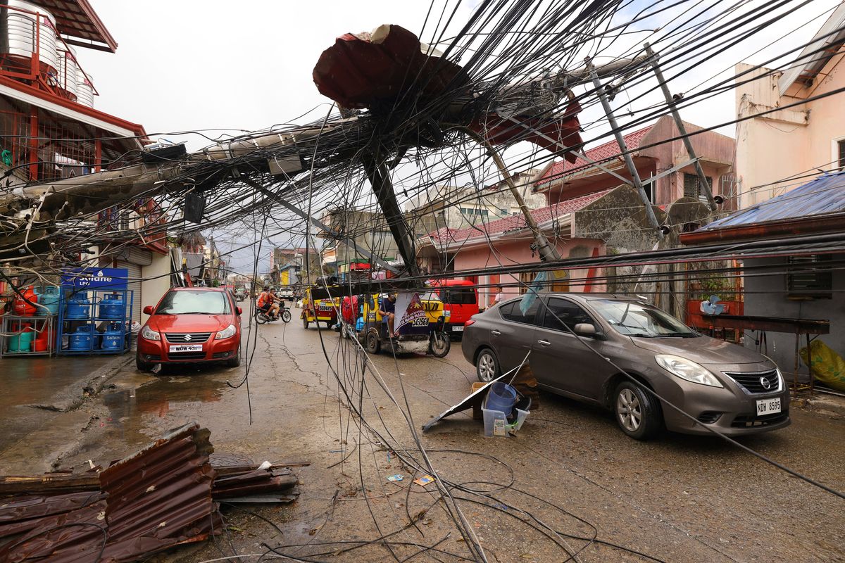 Cars pass by a toppled electrical post due to Typhoon Rai in Surigao city, Surigao del Norte, southern Philippines as power supply remain down on Sunday.  (Jilson Tiu)