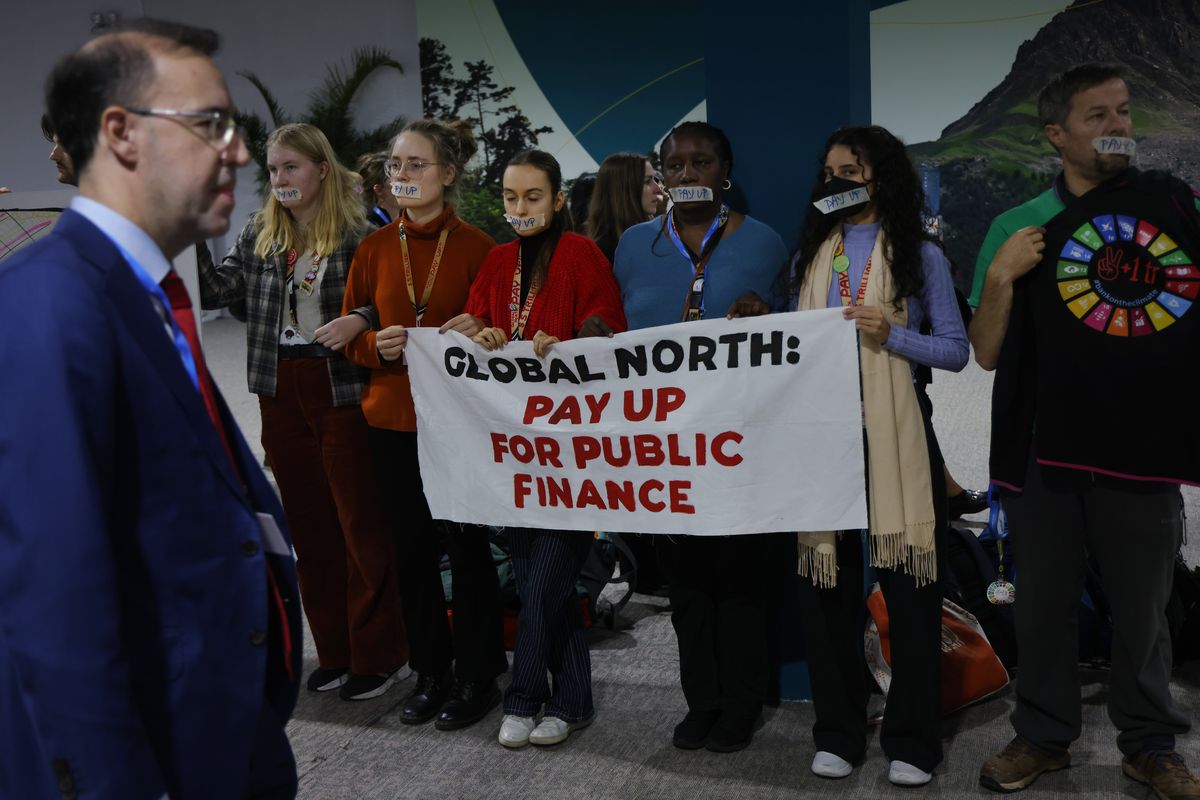 Conference participants walk past activists urging public climate finance for poor countries prior to a first closing plenary on day 12 at the UNFCCC COP29 Climate Conference on Saturday in Baku, Azerbaijan.  (Sean Gallup)