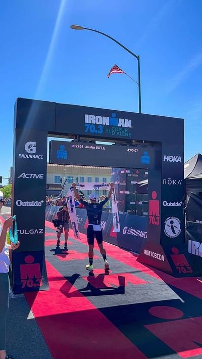 Justine Riele hoists the finish-line tape above his head after winning the 70.3-mile Ironman triathlon in Coeur d’Alene on June 26, 2022.  (Courtesy of Justin Riele)