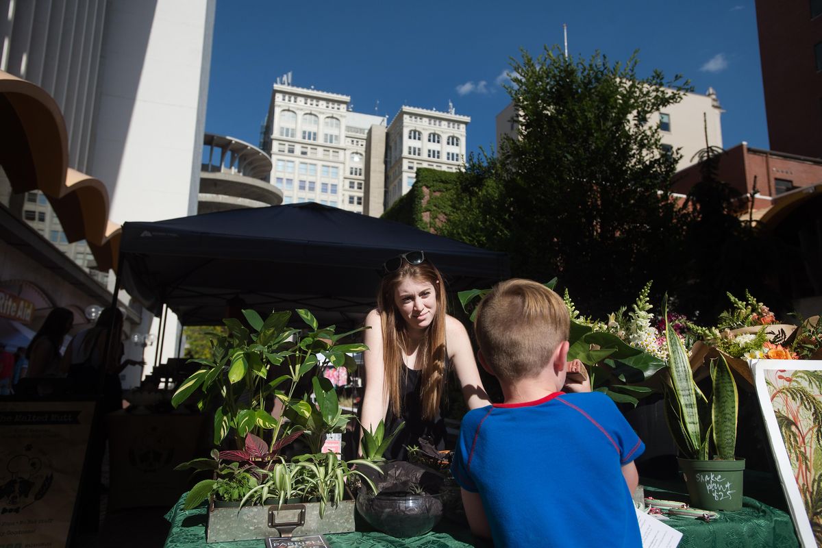 Megan Nikora, 25, with Parish and Grove, answers questions about plants from Banyan Callone, 6, of Spokane on Tuesday  at the Spokane Public Market in downtown Spokane. (TYLER TJOMSLAND/THE SPOKESMAN REVIEW / SR)