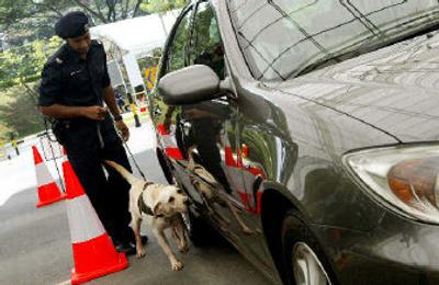 
A police officer holds onto his bomb-sniffing dog as it checks vehicles entering the venue of the International Monetary Fund meeting in Singapore on Monday. 
 (Associated Press / The Spokesman-Review)