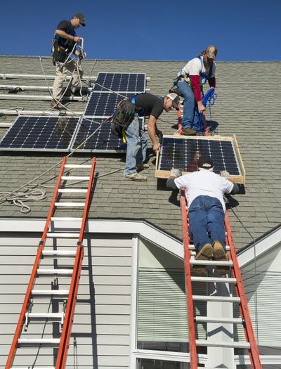 Mike Coulter, project manager with PCI Renewables, slides a solar panel up to workers, left to right, Mark Leo, Billy Truax and Todd Owens, who were installing 75 solar panels onto the roof of the Unitarian Universalist Church of Spokane in October 2012. (File)