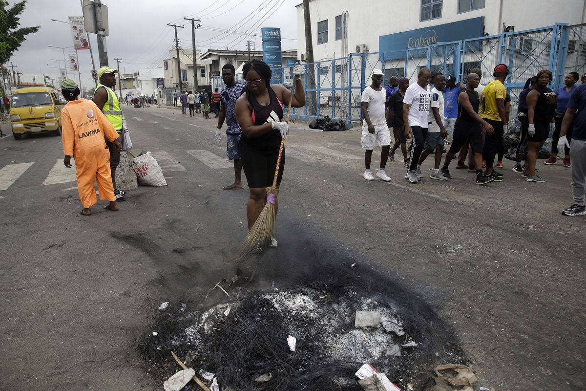 Volunteers sweep burnt out tyres on the roads in Lagos Saturday, Oct. 24, 2020. Nigeria