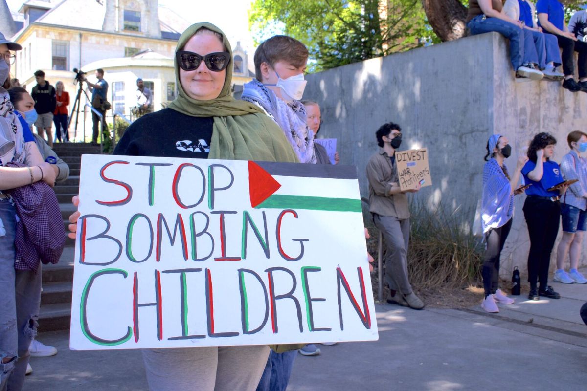 A protester holds a sign that says “stop bombing children” on Thursday on the University of Washington campus.  (Grace Deng/Washington State Standard)
