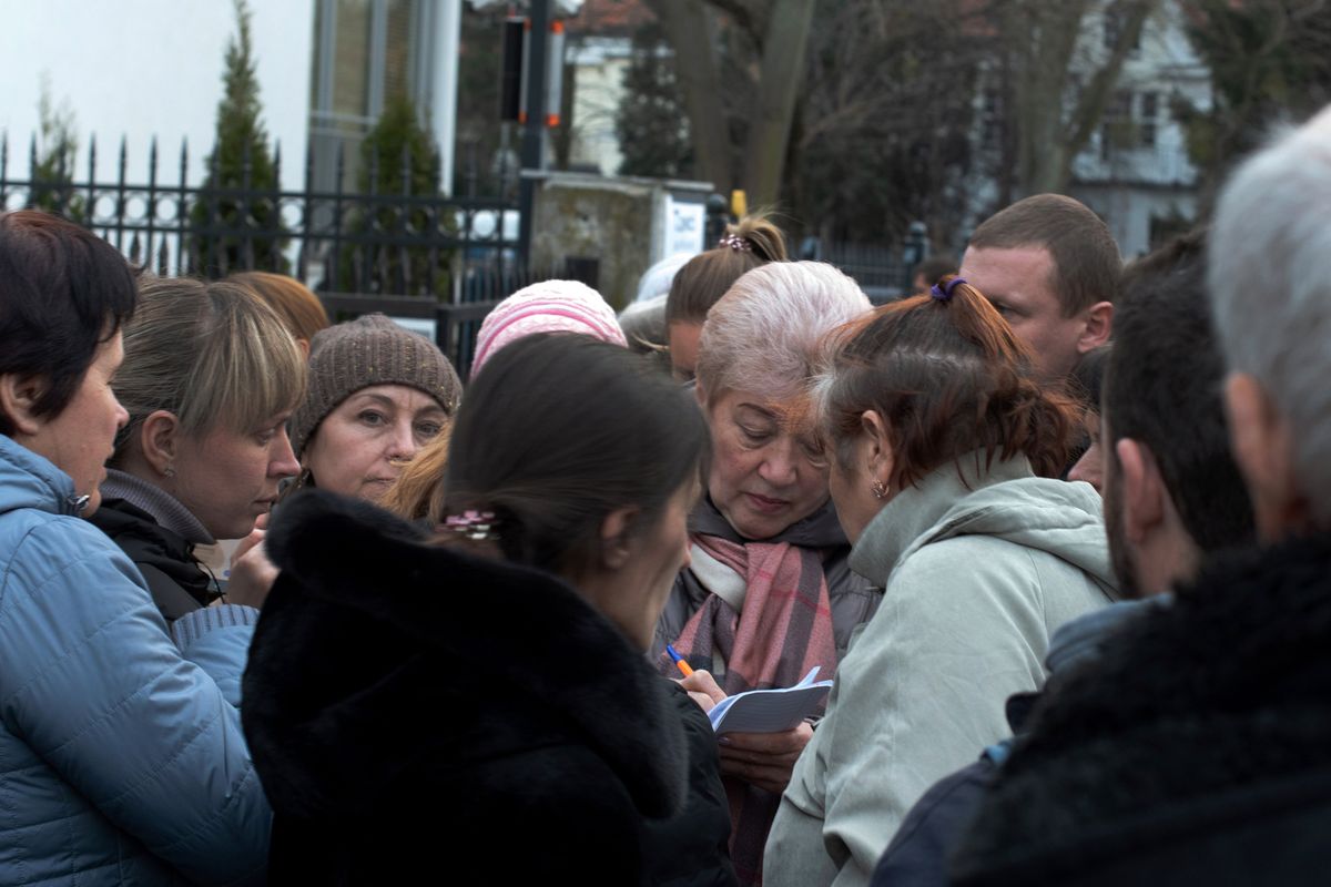 Ukrainian refugees crowd around a Ukrainian government official in front of the country’s consulate office in Warsaw, Poland, on Tuesday. Many refugees don’t have passports, but are applying in hopes of leaving.  (Eli Francovich/The Spokesman-Review)