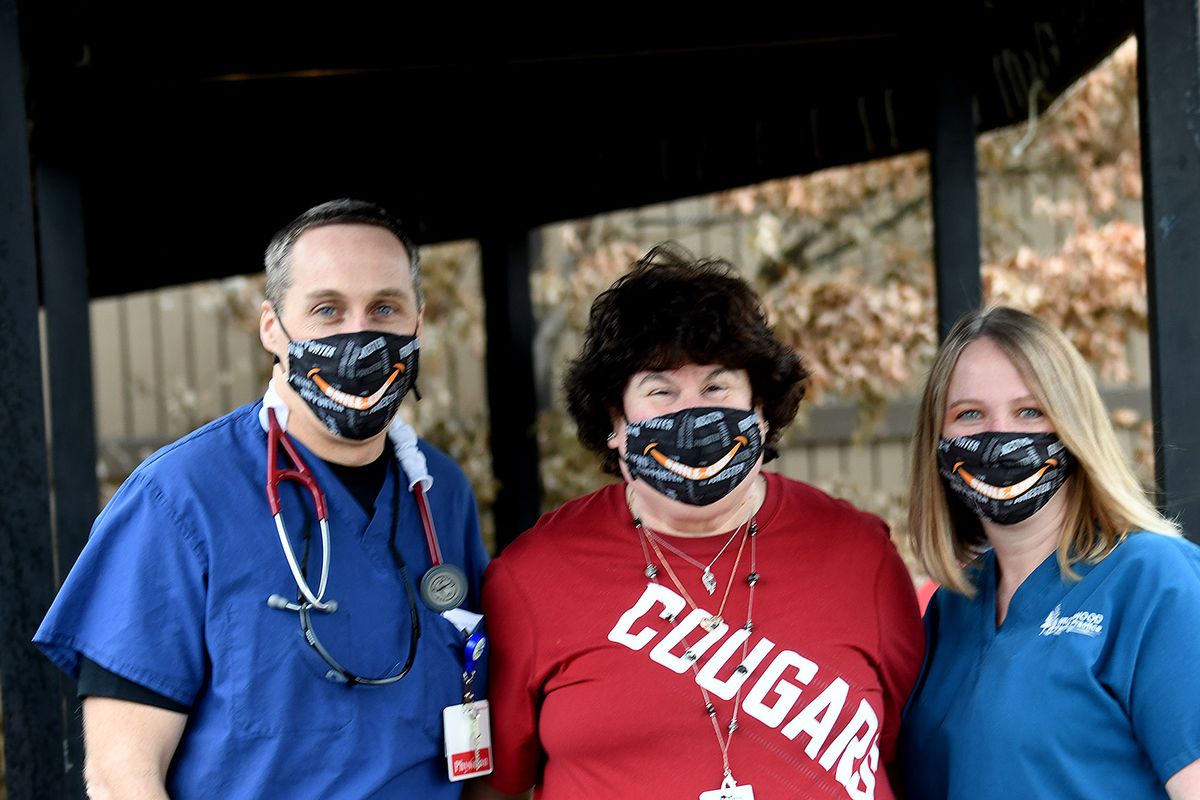 Cheri Hodl, center, with help from Dr. Geoff Emry and admitting representative Amber Tatman, have given away 700 Smile-4 Joe masks in memory of Cheri’s husband, Joe, who died of COVID-19 in August. They are seen Wednesday in Coeur d’Alene.  (Kathy Plonka/The Spokesman-Review)
