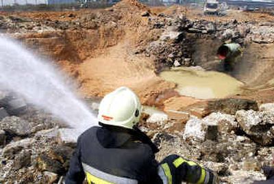 
A firefighter hoses down a large crater made after a gas pipeline exploded Friday in the industrial zone of Ghislenghien, some 20 miles southeast of Brussels.
 (Associated Press / The Spokesman-Review)