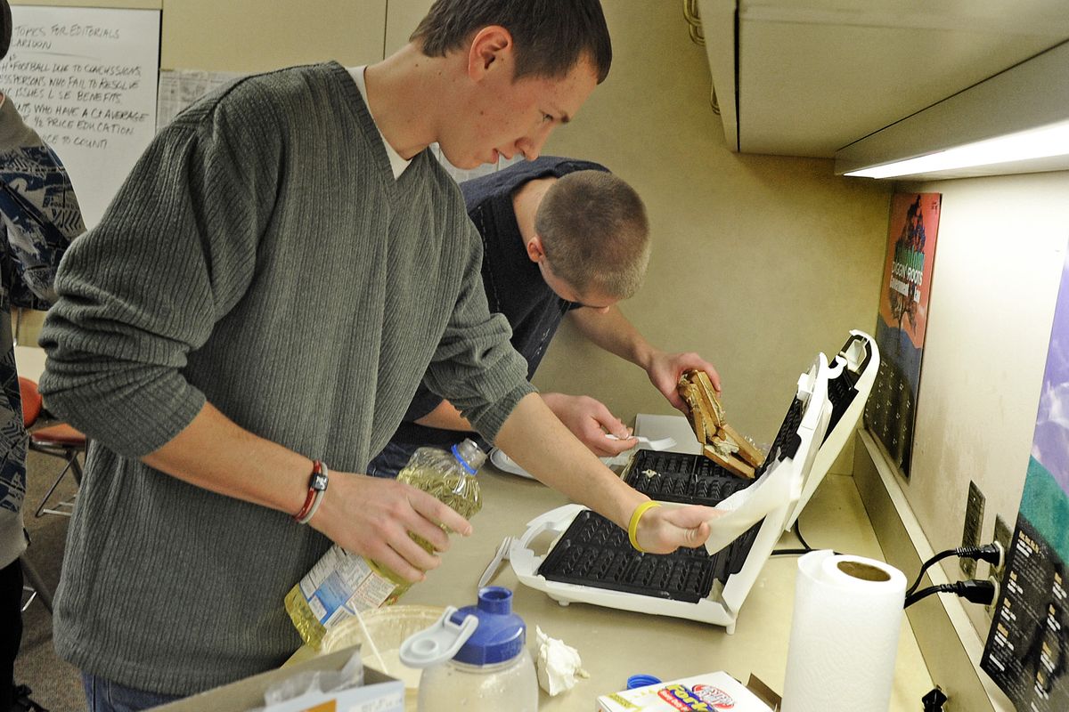 Jared Jefferson, rear, finds out that hot waffle irons and plastic forks don’t mix as he and fellow senior Alex Steinmetz cook waffles for other Lewis and Clark High School students Friday. Looking on is Jesse Madden. (Christopher Anderson)