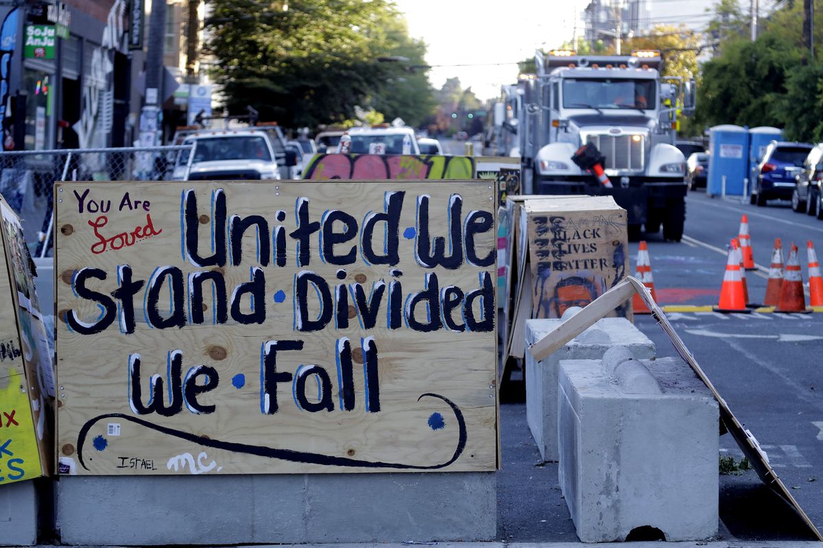 A sign on a barricade reads "United we stand divided we fall," as a truck and other heavy equipment from the Seattle Department of Transportation is staged at the the CHOP (Capitol Hill Occupied Protest) zone in Seattle, Friday, June 26, 2020. Workers arrived with the intention of removing barricades that had been set up in the area and were met with opposition from protesters. Several blocks in the area have been occupied by protesters since Seattle Police pulled back from their East Precinct building following violent clashes with demonstrators earlier in the month. (Ted S. Warren)
