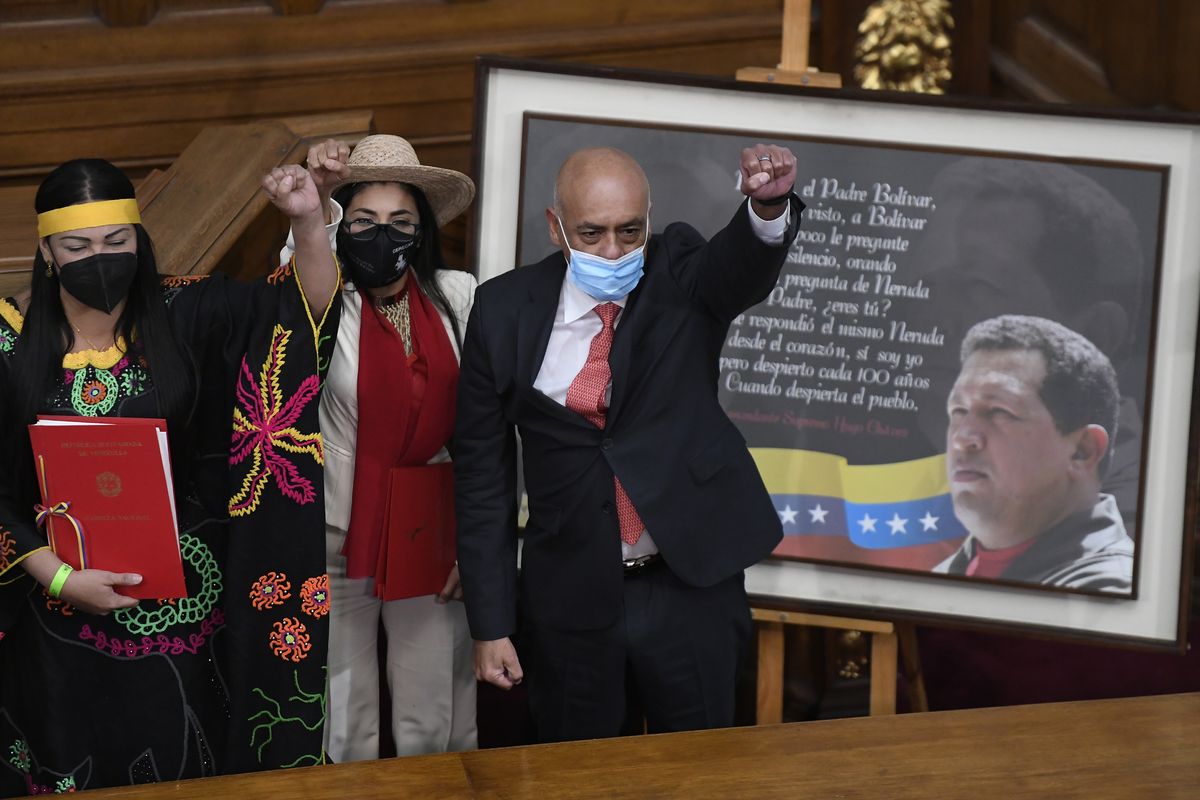 Jorge Rodriguez, right, lifts his fist after being sworn-in as president of the National Assembly, in front of a photo of late President Hugo Chavez, at Congress in Caracas, Venezuela, Tuesday, Jan. 5, 2021. The ruling socialist party assumed the leadership of Venezuela