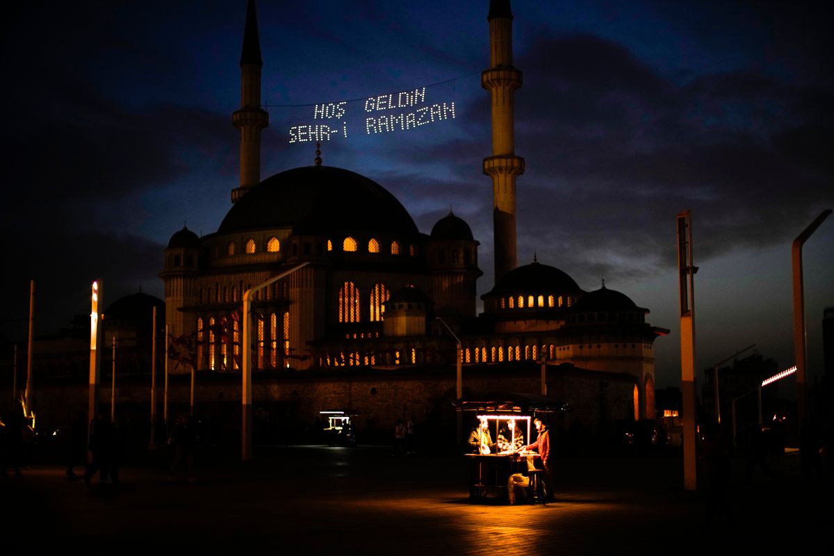 People buy roasted chestnuts next to Taksim mosque as the sun sets during the first day of the Muslim holy fasting month of Ramadan, in Istanbul, Turkey, Saturday, April 2, 2022. Lights on top read in Turkish: "Welcome Sehr-i Ramadan".  (Francisco Seco)