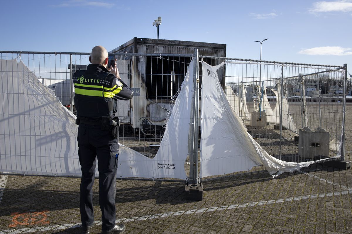 A police officer takes pictures of a burned-out coronavirus testing facility on Jan. 24 in the fishing village of Urk in the Netherlands after it was set on fire the night before by rioting youths protesting on the first night of a nationwide curfew. (Peter Dejong)