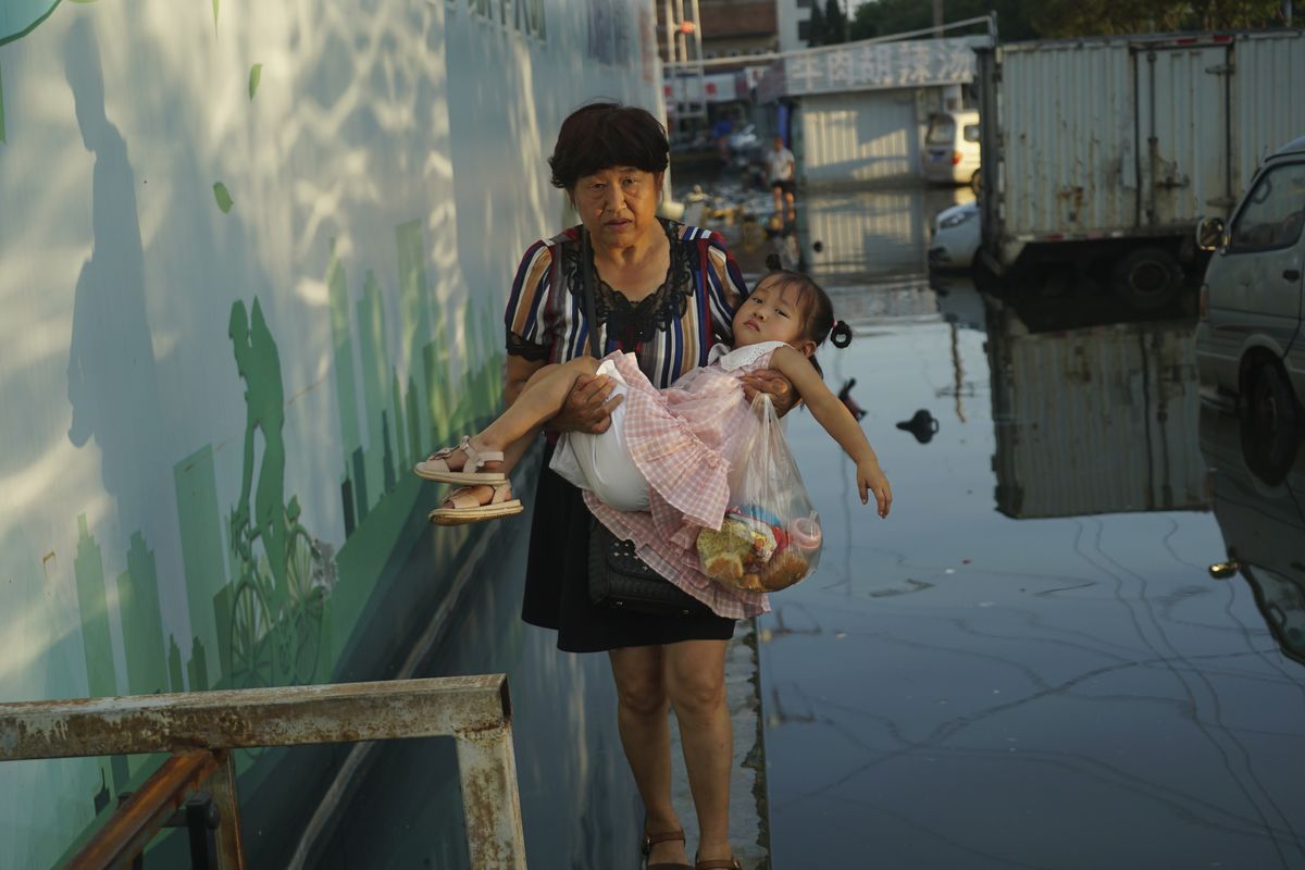 A woman carries a child in her arms as she walks on a curb above floodwaters Monday in Xinxiang in central China’s Henan Province. (Dake Kang)