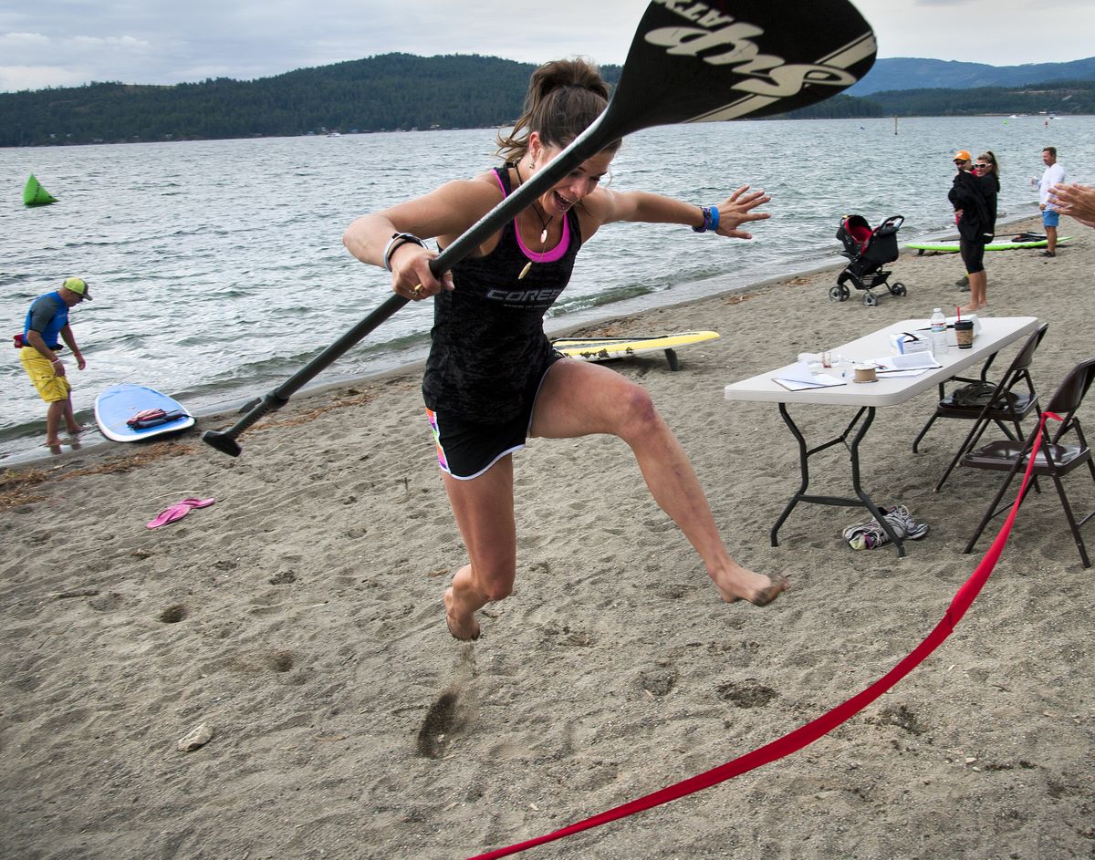 Grace Robison, 20, of Coeur d’Alene, leaps over the finish line tape after competing in the first Coeur d’SUP Stand Up Paddleboard Races & Festival at City Beach on Saturday. (PHOTOS BY DAN PELLE)