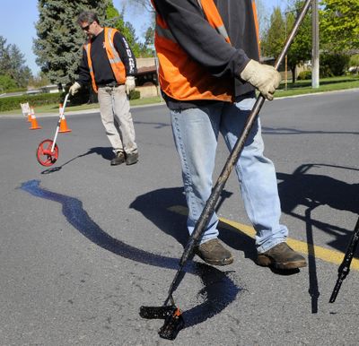 Troy Binsfield, left, measures the amount of product used to seal street cracks on 37th Avenue near Manito Boulevard in Spokane on Friday. John Britton, right, spreads the tar into the cracks. (Dan Pelle)