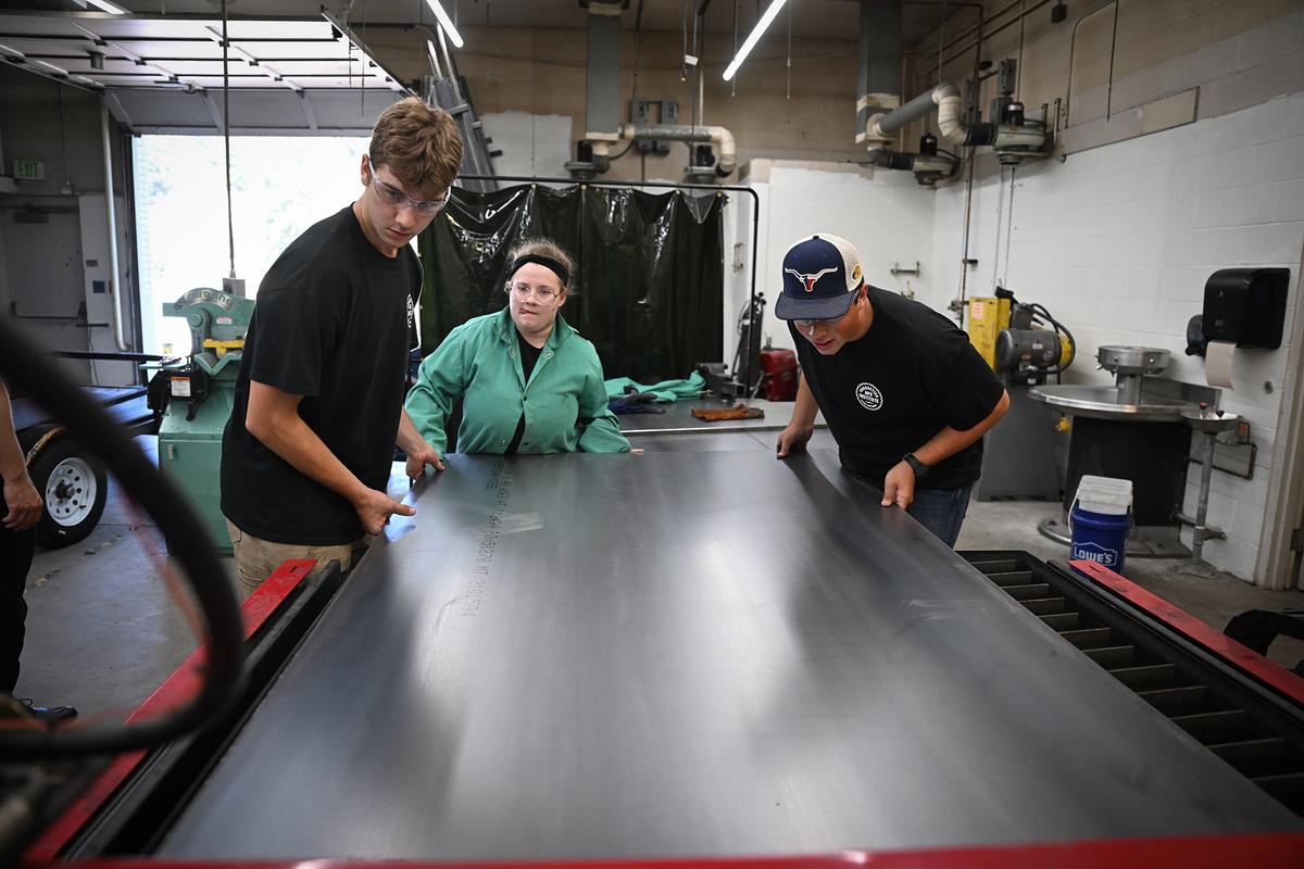High school students Wilson Hash, left, Alexandria Schaffer and Nick McLaughlin load a sheet of steel into the CNC plasma cutter inside the metal shop at East Valley High School Friday. (Jesse Tinsley/The Spokesman-Review)