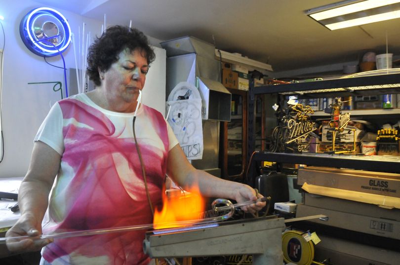 Dana Eberly, of Spokane Valley, heats a glass tube with a special torch setup before bending it. She said plastic signs took over in the 1970s, but neon came back in the 1980s. Now LED lights are popular. (Jesse Tinsley)