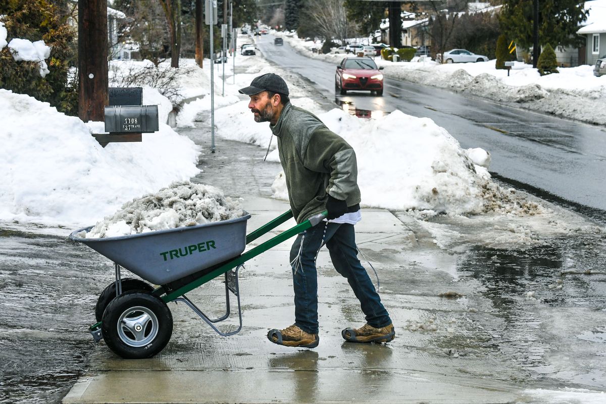 Mike Canto hauls away his seventh wheelbarrow load of snow and ice from a berm he cleared away from his driveway leading to 37th Avenue Friday in Spokane.  (DAN PELLE/THE SPOKESMAN-REVIEW)