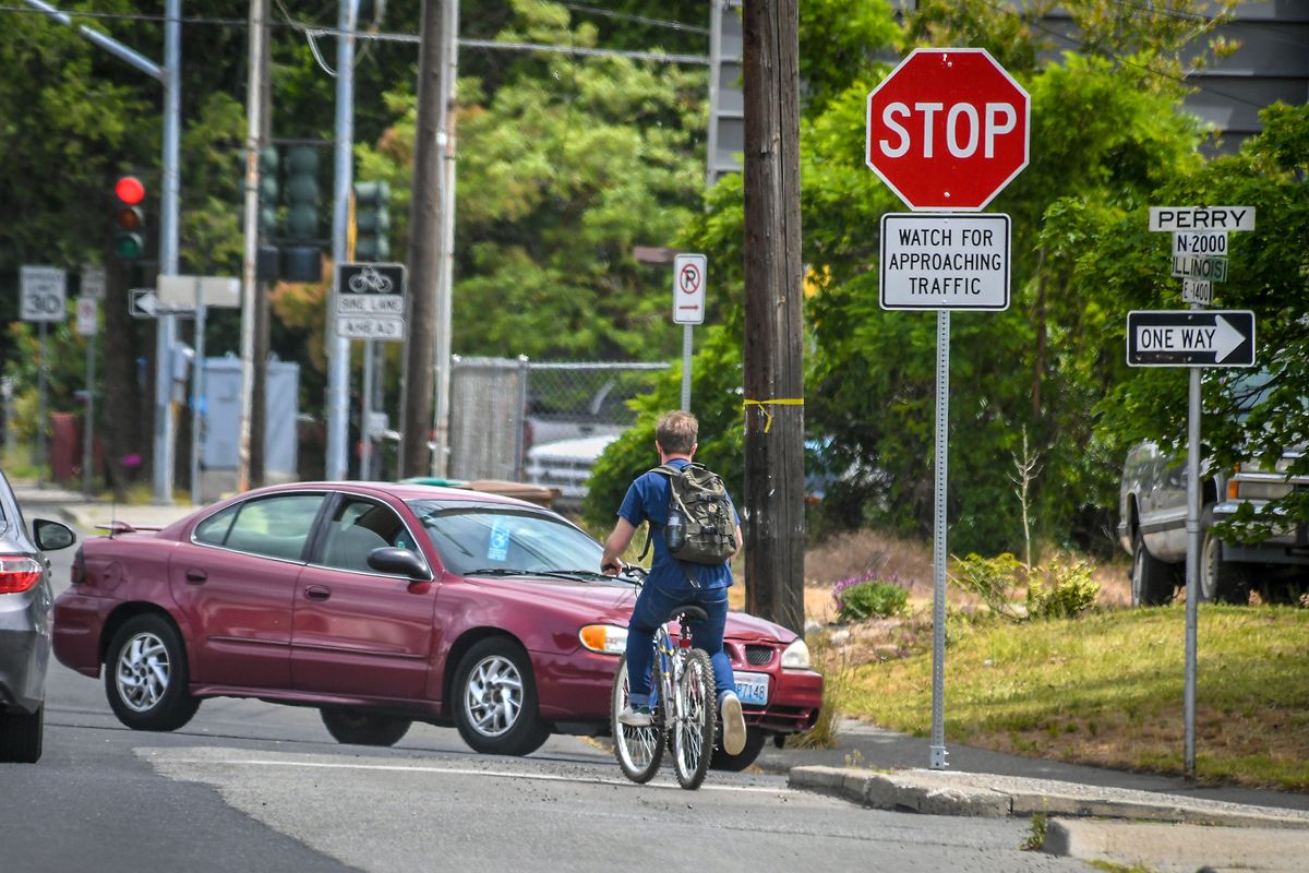 A cyclist pauses his ride to wait for traffic at the corner of Illinois Avenue and Perry Street on Thursday in Spokane. Plans for more biking-friendly options at Illinois and Perry could soon be coming to West Central as well.   (DAN PELLE/THE SPOKESMAN-REVIEW)