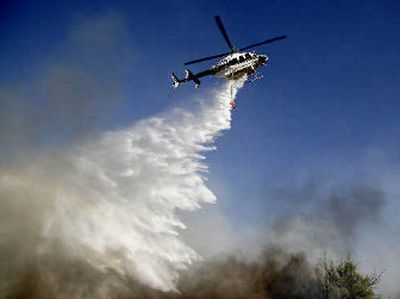 
A helicopter drops water on a wildfire in Morongo Valley, Calif., on Wednesday. It began spreading after a house caught fire. 
 (Associated Press / The Spokesman-Review)