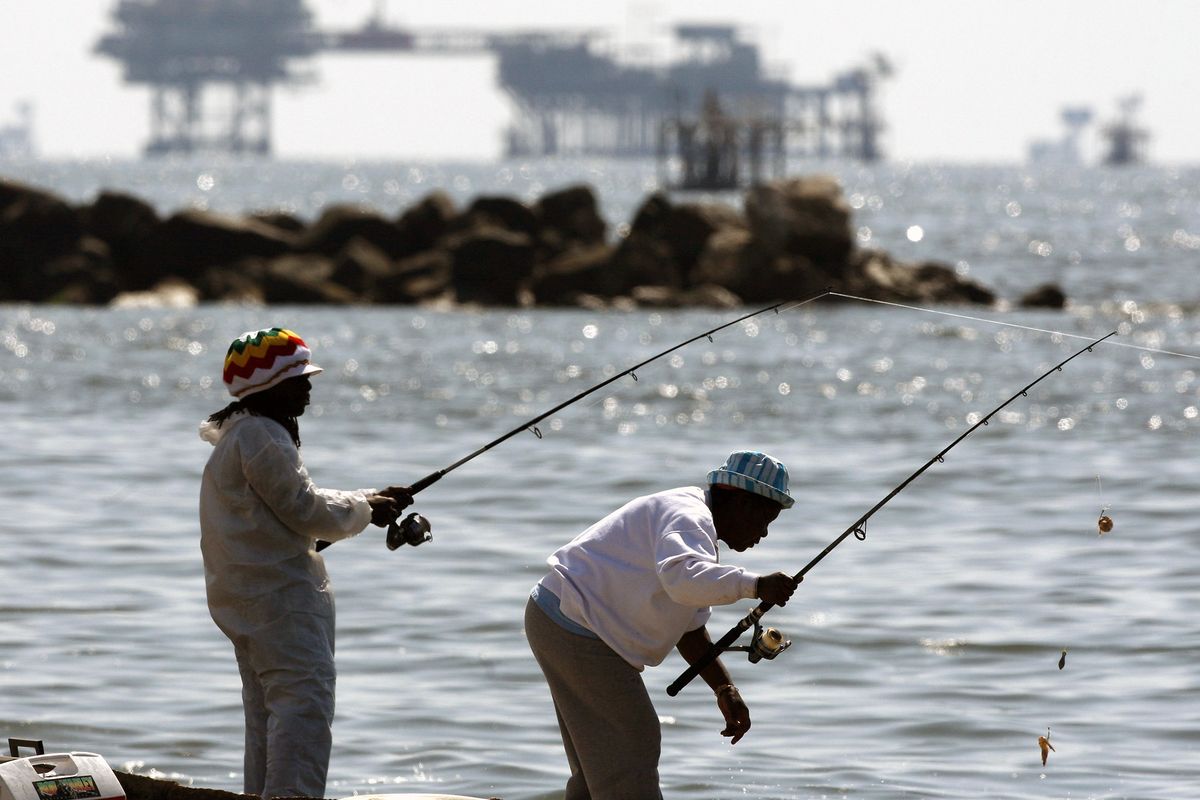 An oil drilling platform stands offshore in the Gulf of Mexico as people fish Wednesday in Port Fourchon, La. Associated Press photos (Associated Press photos)