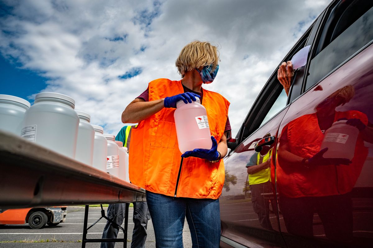 Volunteer Ann Marie Dorn with STCU, hands a jug of disinfectant to a small business owner during a drive-thru PPE distribution, Tues., June 30, 2020, at the Spokane County Fairgrounds. After county commissioners allocated $2 million to fund PPE for businesses, the county and Greater Spokane Inc. with volunteers distributed hand sanitizer, disinfectant, face masks to hundreds of businesses that need it to reopen or stay open during the COVID-19 pandemic. (Colin Mulvany/THE SPOKESMAN-REVIEW)